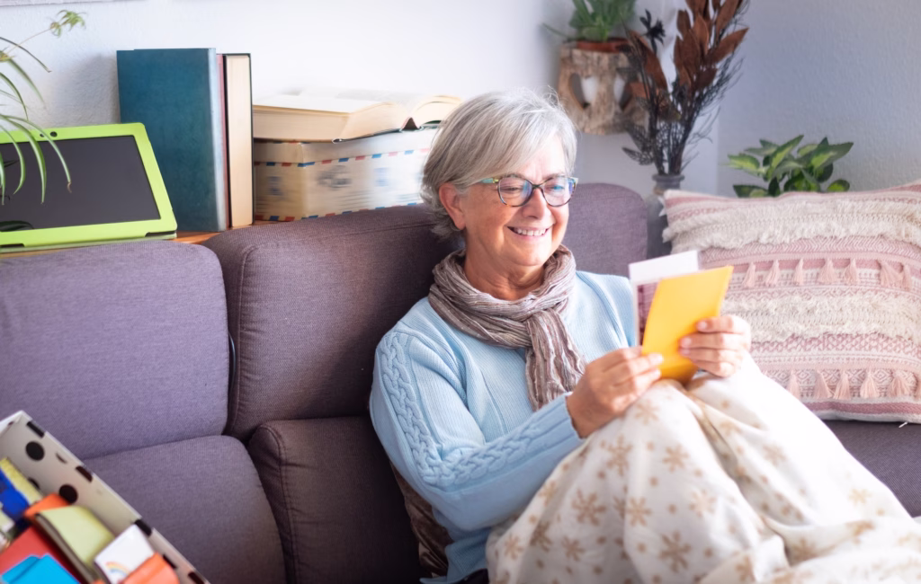 Attractive old lady gray haired sitting on sofa at home remembers the past looking at old photograph
